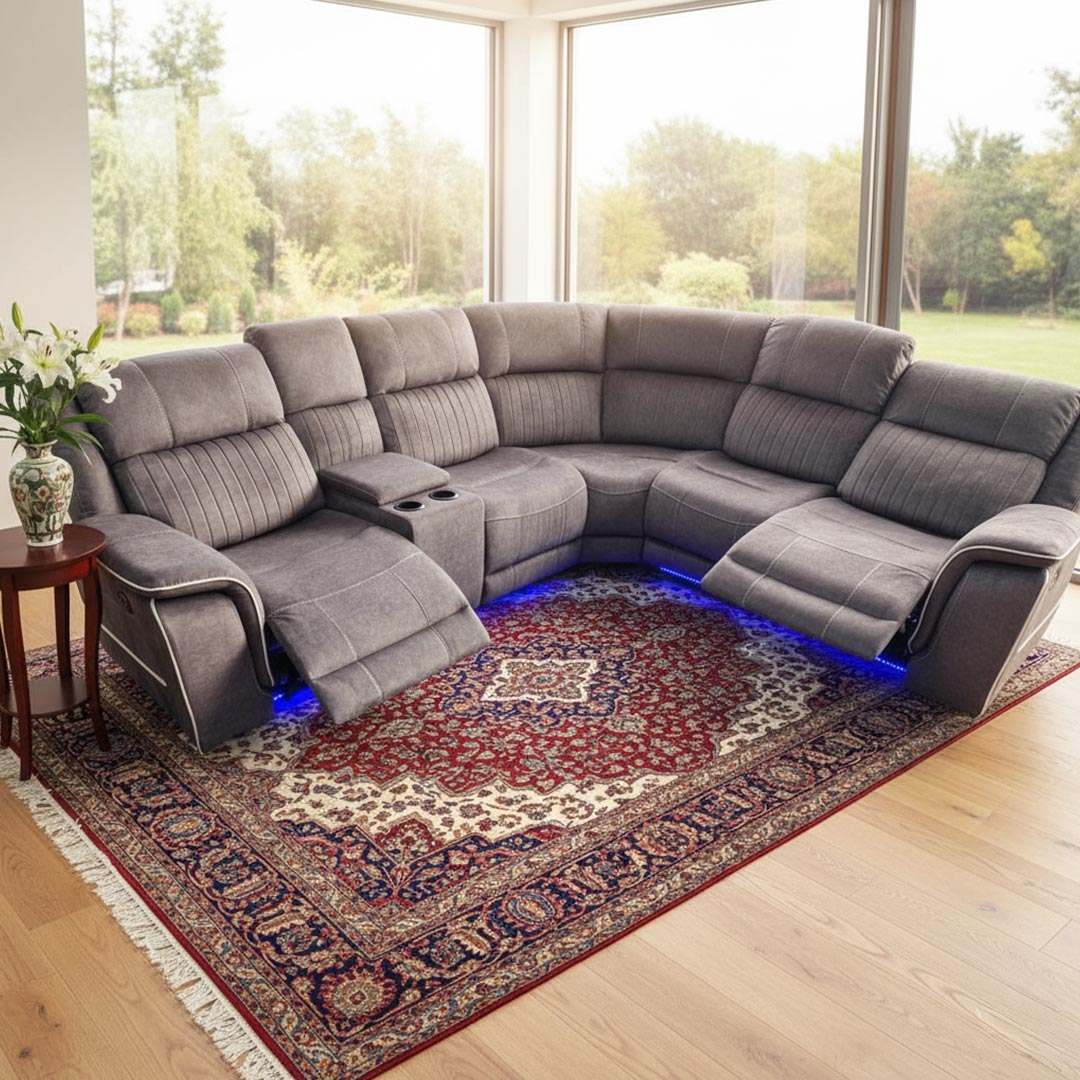 Gray sectional sofa with reclining seats on a patterned rug in a bright room.